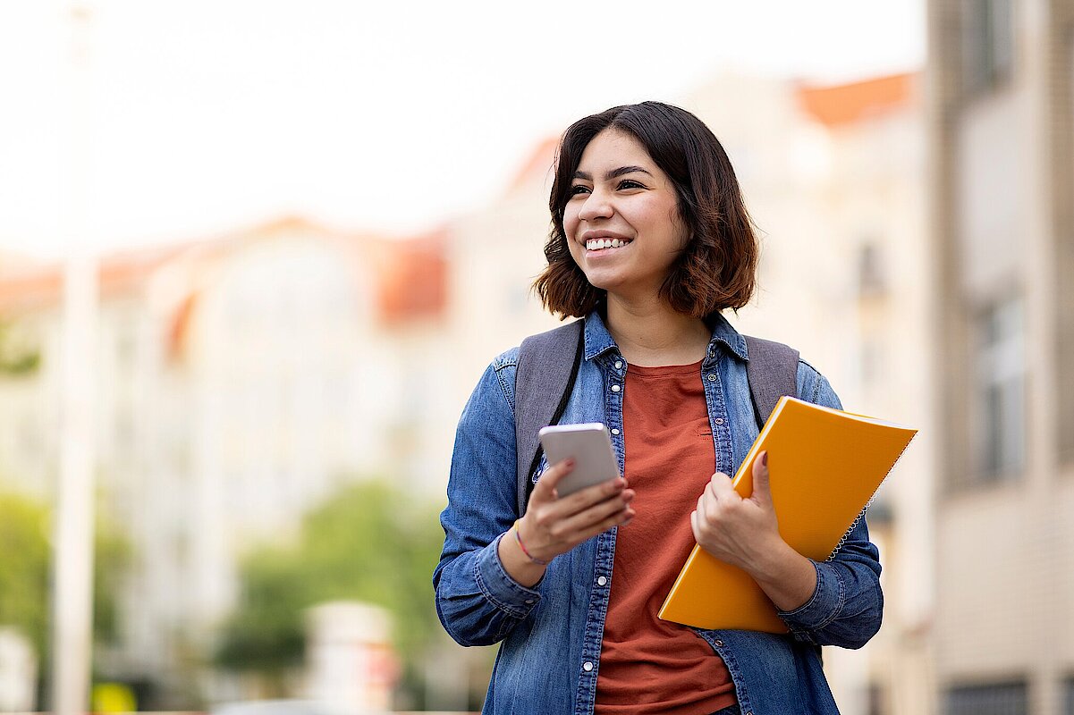 Cheerful,Arab,Female,Student,With,Smartphone,And,Workbooks,Standing,Outdoors,